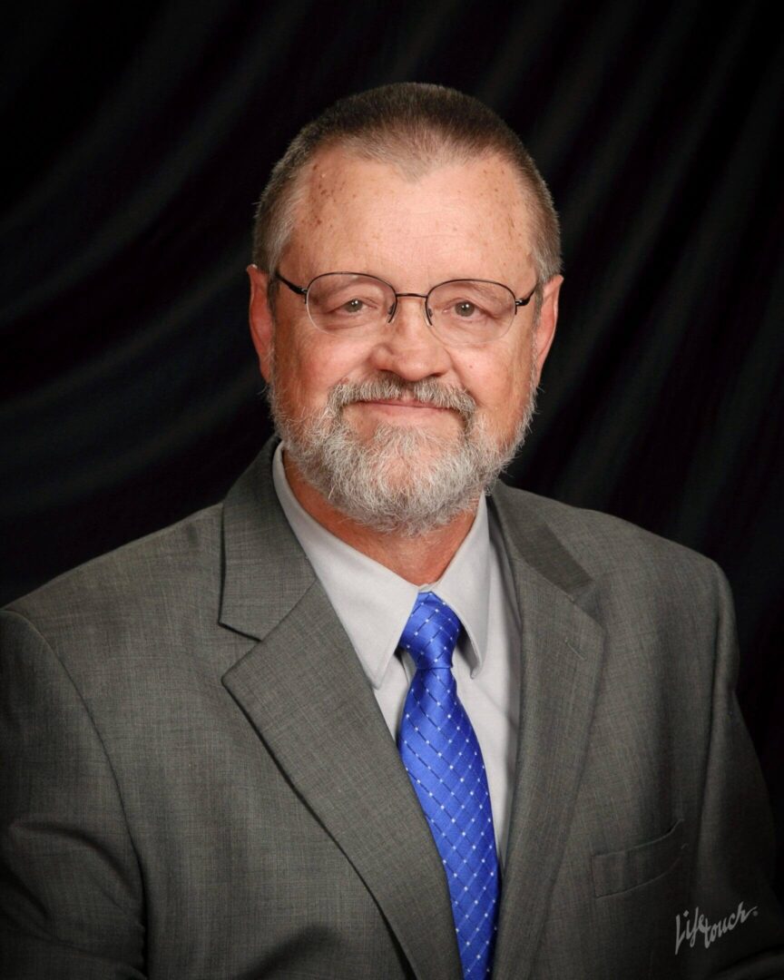 Professional man in a suit and blue tie against a black background.