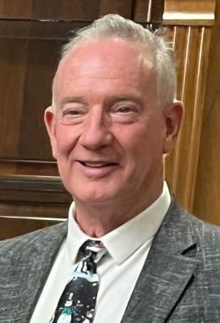 Smiling older man in a gray suit and striped tie indoors.